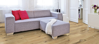 Im Wohnzimmer ist Parkett in Langdielen-Optik verlegt. Dazu passt ein Ecksofa mit bunten Kissen.